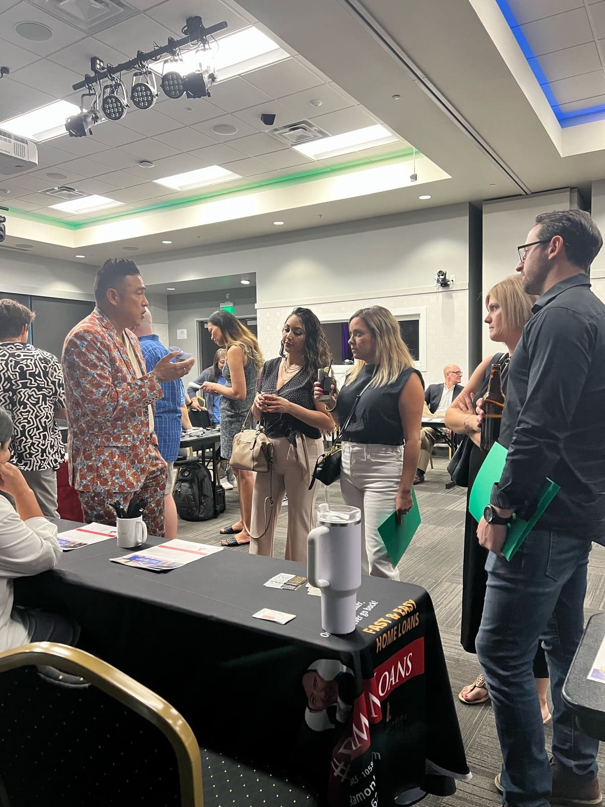 Group of professionals networking and conversing at an indoor business event with branded table