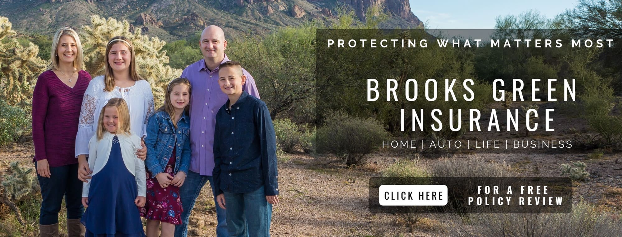 Family of five standing in desert landscape with mountains and cacti, smiling at camera