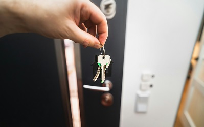 Hand holding silver keys in front of an open door