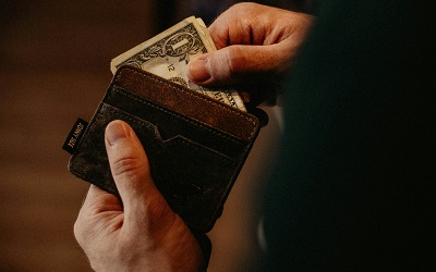 Person holding open an empty brown leather wallet showing no money inside