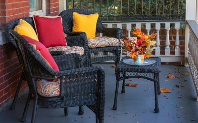 Black wicker patio furniture with colorful pillows and fall flowers on a covered porch
